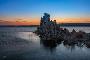 A large Tufa stands silently in the lake as sunrise approaches with a fire smoke filled horizon